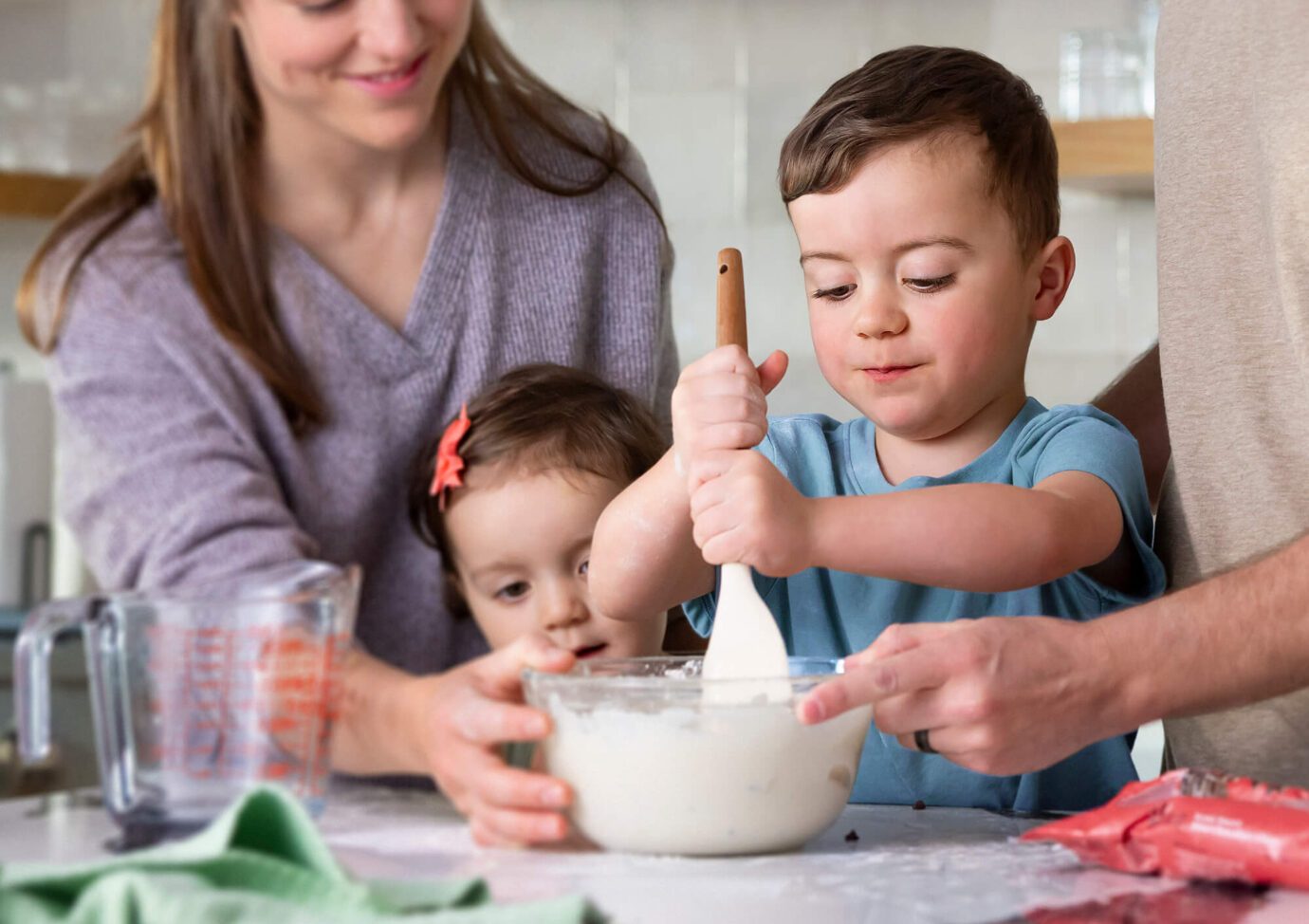 Child mixing batter in kitchen with family