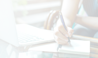 person writing in notebook next to laptop computer